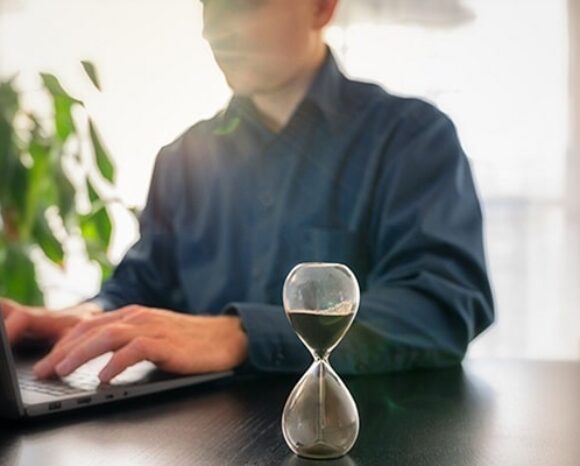 Mann arbeitet neben Sanduhr am Laptop