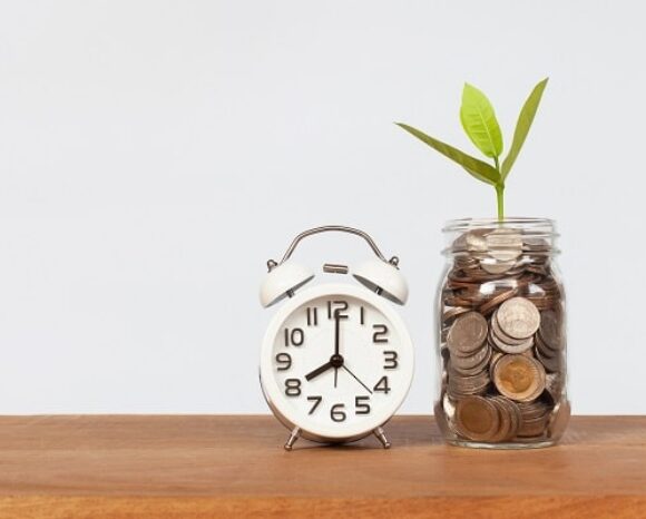 Wecker neben Glas mit angespartem Geld