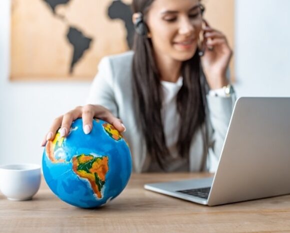 Personalerin arbeitet am Laptop und legt eine Hand auf einen Globus