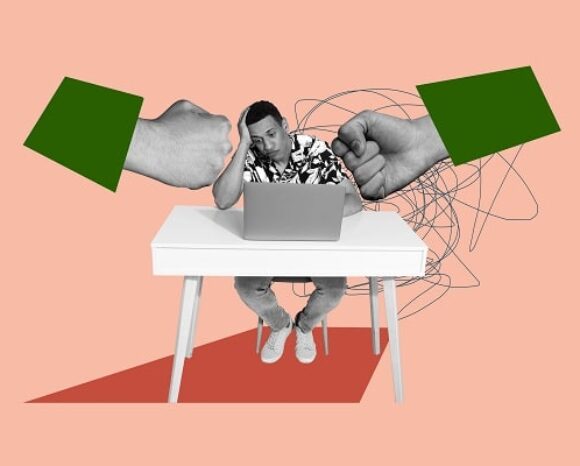 Mann arbeitet im Homeoffice und wird von zwei großen Fäusten geboxt