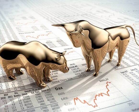 Zwei goldene Figuren – ein Bär und ein Bulle – stehen auf einer Finanzzeitung mit Börsendaten und Charts. Der Bulle wirkt stark und angriffslustig und symbolisiert einen Bullenmarkt, während der Bär zurückhaltender wirkt und einen Bärenmarkt repräsentiert.