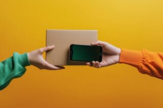 Eine Hand überreicht einer anderen Hand eine Box und ein Handy. Auf dem Weg hin zu einer digitalen Zustellung.