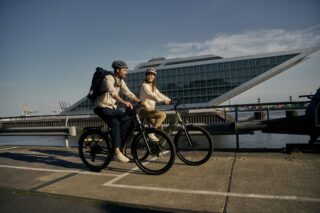 Ein Mann und eine Frau fahren mit eine geleasten Fahrrad am Hafen entlang.