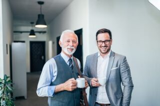 Ein älterer und ein jüngerer Kollege stehen zusammen beim Reverse Mentoring.