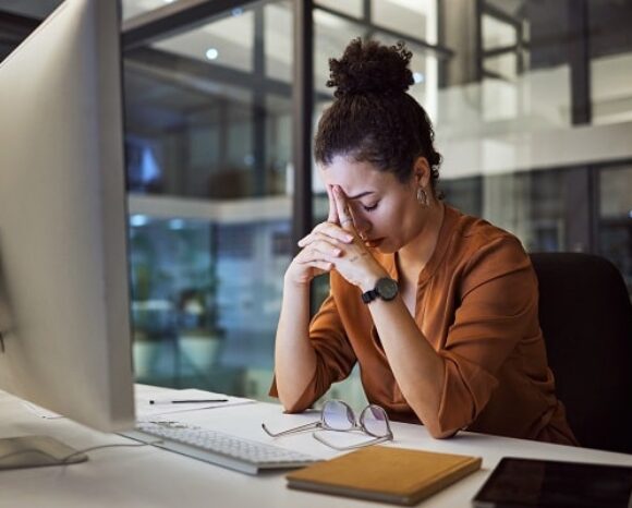 Gestresste Mitarbeiterin stützt den Kopf an ihrem Arbeitsplatz in die Hände