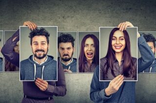 Ein Mann und eine Frau halten Poster mit Gesichtsausdrücken hoch, auf den verschiedenen Bildern sind verschiedene Persönlichkeitsmerkmale und Emotionen zu erkennen.