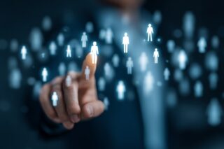 Finger eines Mannes tippt auf ein digitales Symbol einer Person in einer virtuellen Benutzeroberfläche zur Mitarbeiterauswahl
