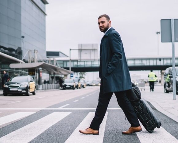 Ein Mann zieht seinen Koffer über einen Zebrastreifen und geht auf Dienstreise.