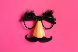 Fake-Brille und Nase plus Schnurrbart liegen auf pinkem Untergrund