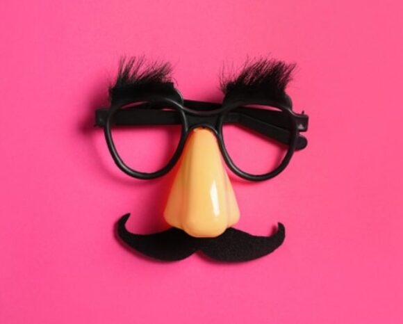Fake-Brille und Nase plus Schnurrbart liegen auf pinkem Untergrund