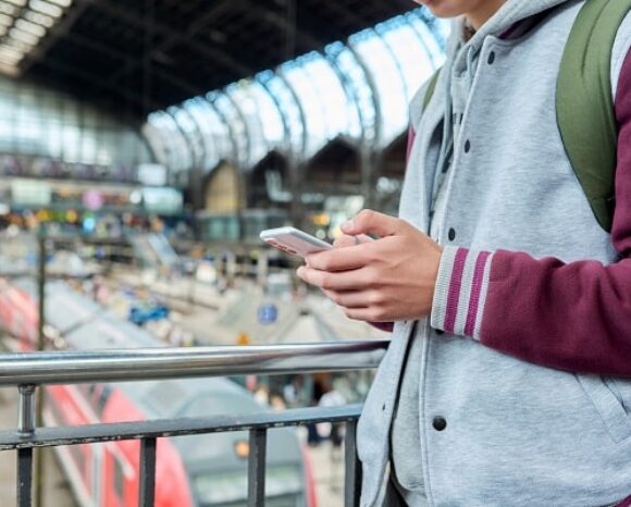 Mann steht am Bahnhof und schaut auf sein Handy mit dem Deutschlandticket.