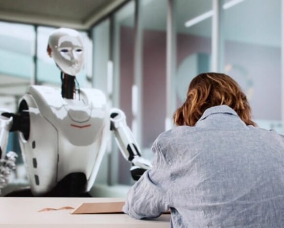 Frau sitzt im Bewerbungsgespräch mit Roboter/Künstlicher Intelligenz