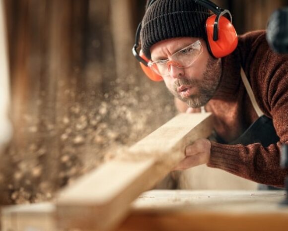 Tischler pustet Sägespäne von Holzstück