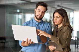 Mann und Frau reden und schauen auf einen Laptop, den der Mann in der Hand hält