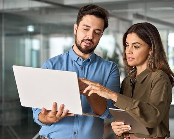 Mann und Frau reden und schauen auf einen Laptop, den der Mann in der Hand hält
