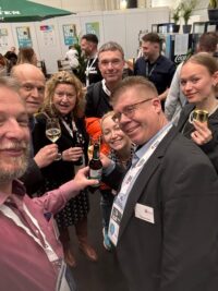 Thomas Buck stößt mit verschiedenen Bekannten und Messebesuchern auf dem Messestand an.