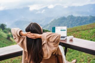 Junge Frau arbeitet am Laptop und schaut auf die Berge.