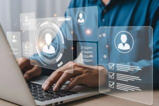 Person arbeitet an einem Laptop mit schwebenden digitalen Symbolen und Profil-Icons, die Personal- oder Payroll-Daten darstellen. Das Bild steht sinnbildlich für moderne, automatisierte Entgeltabrechnung und digitale HR-Prozesse.