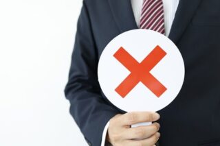 Ein Mann hält rundes Schild mit x hoch, was Ablehnung symbolisiert.