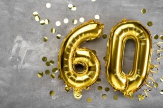 Die Zahl 60 liegt als Luftballon in Mitten von Glitzer auf dem Boden.