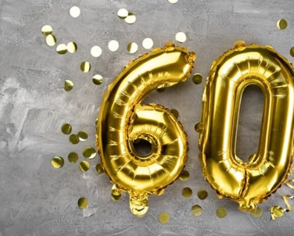 Die Zahl 60 liegt als Luftballon in Mitten von Glitzer auf dem Boden.