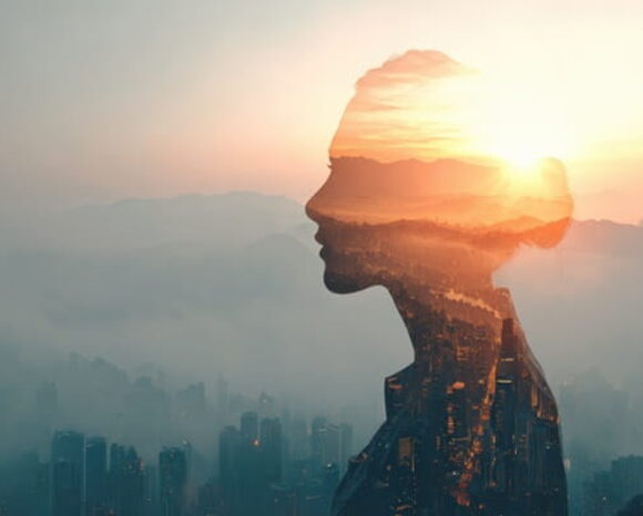 Frau blickt in die Ferne, hinter ihr liegt das Tal im Nebel und die Sonne geht auf