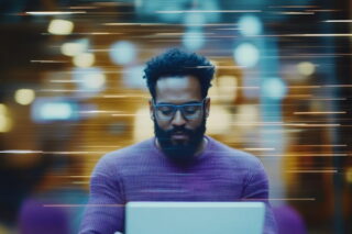 Mann im lilafarbenen Pullover arbeitet am Laptop und steht für die Zukunft der Arbeit