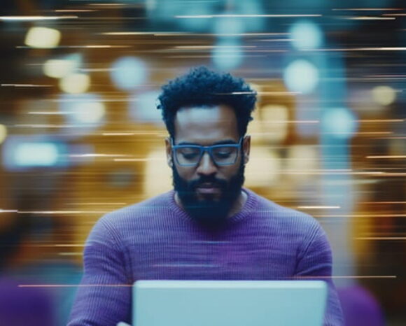 Mann im lilafarbenen Pullover arbeitet am Laptop und steht für die Zukunft der Arbeit