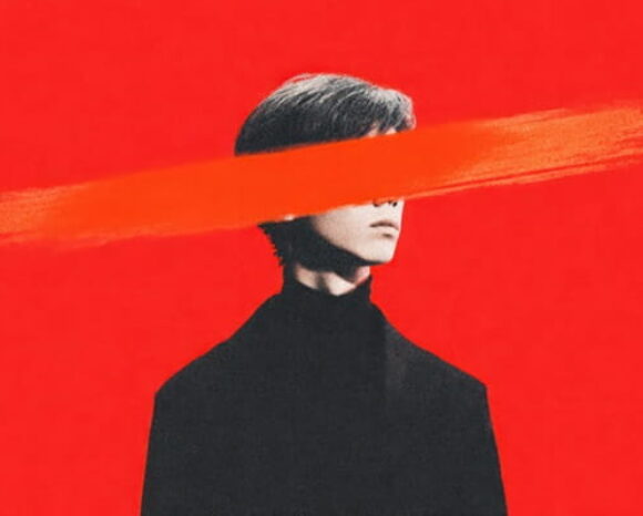 Mann im dunklen Anzug vor rotem Hintergrund, wobei Augenpartie durchgestrichen ist