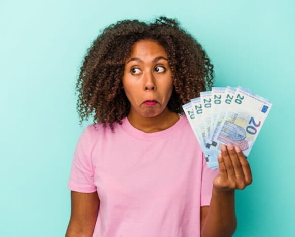 Frau mit lockigen Haaren hält Geldscheine in der Hand und macht ein unwissendes Gesicht