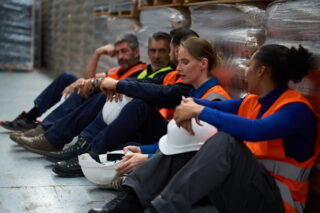 Überstunden: Lagermitarbeiter sitzen erschöpft auf dem Boden