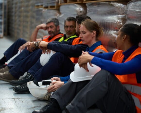 Überstunden: Lagermitarbeiter sitzen erschöpft auf dem Boden