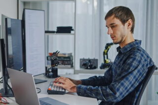 Mann arbeitet an mehreren Bildschirmen und beachtet die Vorgaben zur Cybersicheit