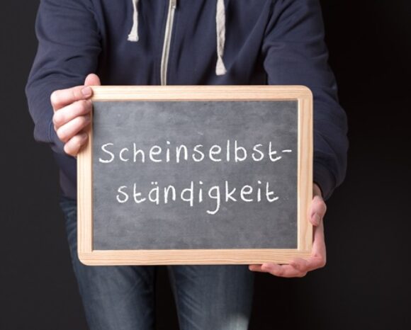Mann hält Tafel hoch, auf der Scheinselbstständigkeit steht