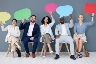 Menschen sitzen nebeneinander und halten bunte Sprechblasen hoch, die Feedback symbolisieren