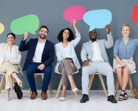 Menschen sitzen nebeneinander und halten bunte Sprechblasen hoch, die Feedback symbolisieren