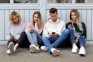 Junge Menschen sitzen auf dem Boden und schauen auf ihr Handy