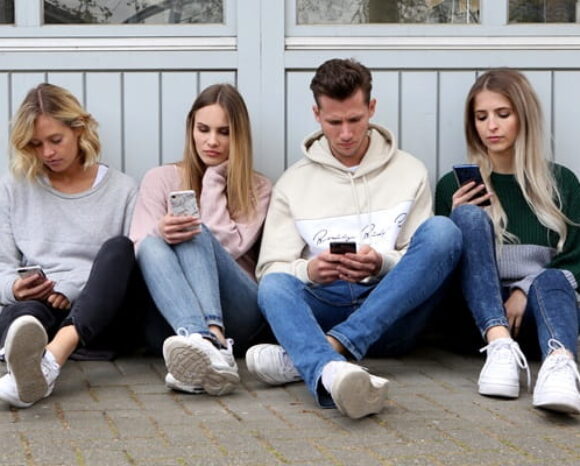 Junge Menschen sitzen auf dem Boden und schauen auf ihr Handy