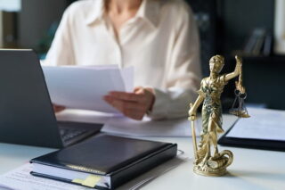 Frau bearbeitet Blätter zum Reformpaket am Laptop, neben ihr steht die Justitia