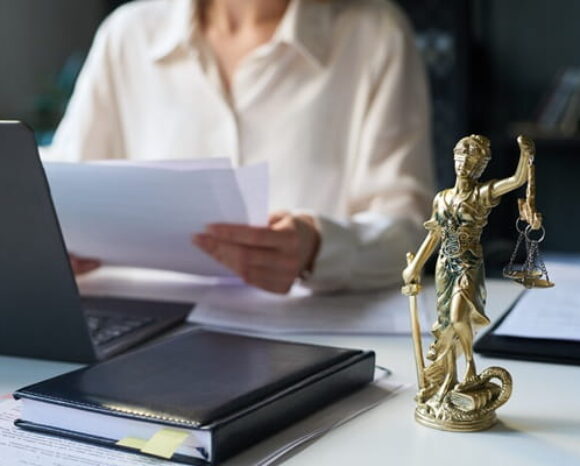 Frau bearbeitet Blätter zum Reformpaket am Laptop, neben ihr steht die Justitia