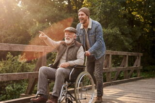 Mann schiebt seinen Vater im Rollstuhl durch die Herbstlandschaft