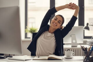Mitarbeiterin streckt sich im Büro und hat gute Laune
