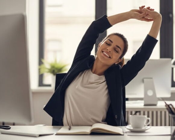 Mitarbeiterin streckt sich im Büro und hat gute Laune