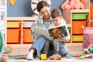 Frau liest im Kindergarten einem Jungen ein Buch vor