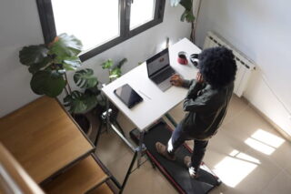 Frau arbeitet am Laptop und läuft auf Laufband