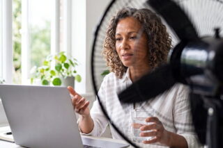 Frau arbeitet im Büro am Laptop mit Ventilator neben sich