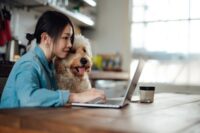 Junge Frau arbeitet am Küchentisch, neben ihr sitzt ihr Hund