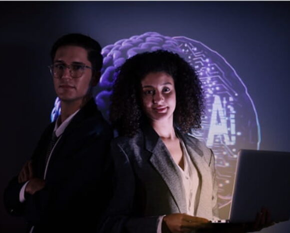 Mann und Frau schauen in die Kamera im Halbdunkeln, hinten ist eine Projektion mit AI