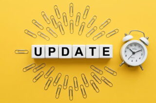 Auf gelbem Untergrund steht in der Mitte Update, umrandet von Büroklammern, neben einem Wecker