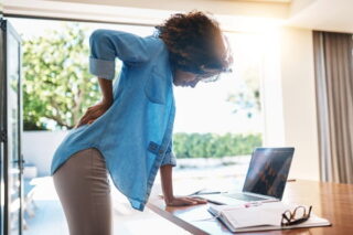 Frau leidet im Homeoffice an Rückenschmerzen